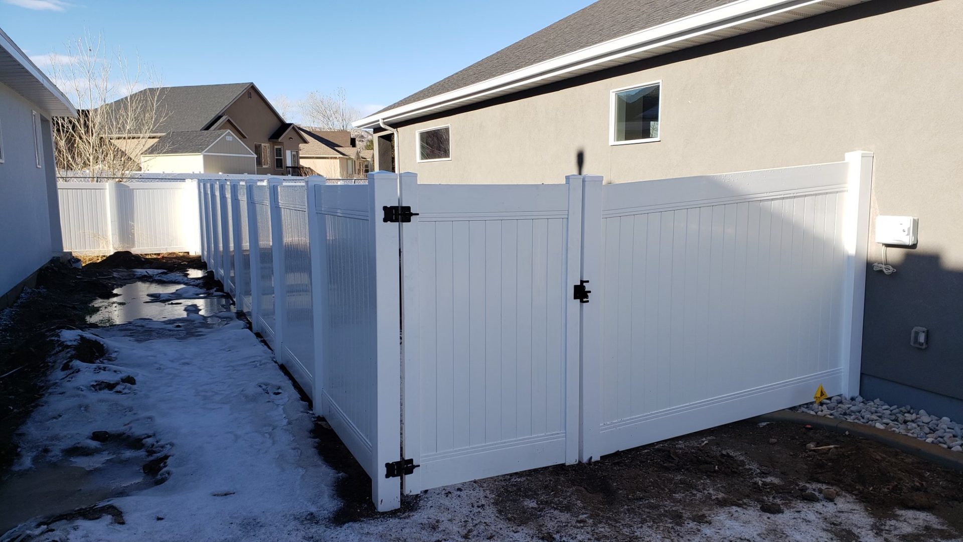 White vinyl privacy fence and gate beside a stucco home